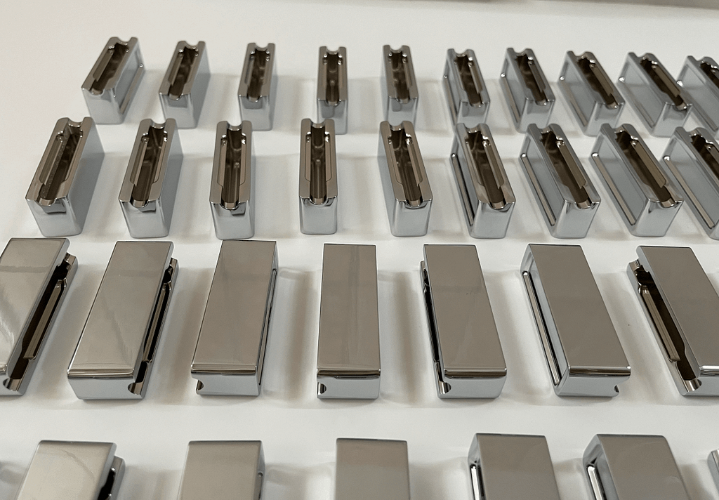 Batch of high-polish mirror finish CNC machined metal housings organized on a white inspection tray.