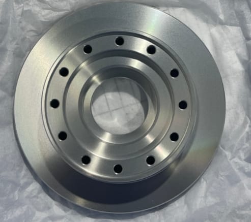 Precision CNC turned aluminum flange with bead blasted finish sitting on protective packaging paper.