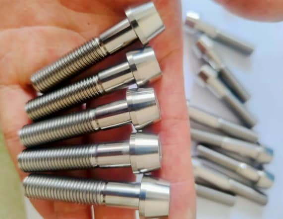 Hand holding custom CNC machined Grade 5 Titanium fasteners with tapered heads and rolled threads.