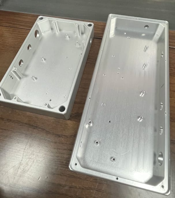 Two raw CNC machined aluminum electronics enclosures showing internal standoffs and thin walls.