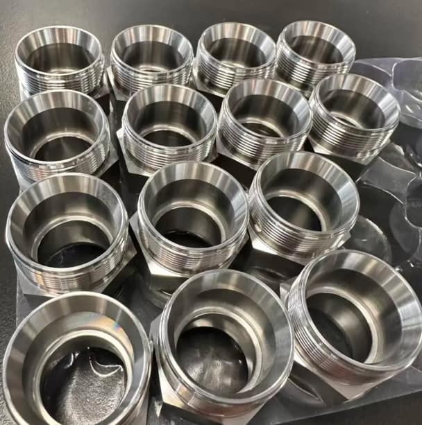 Batch of precision CNC turned stainless steel hydraulic fittings with thick walls and external threads on a tray.